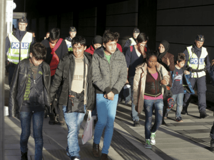 A group of migrants off an incoming train walk down a platform as they are accompanied by