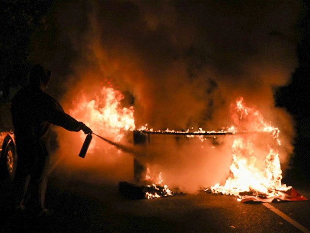 A person uses a fire extinguisher to put out a burning barricade in Philadelphia on October 27, 2020, during a protest over the police shooting of 27-year-old Black man Walter Wallace. - Hundreds of people demonstrated in Philadelphia late on October 27, with looting and violence breaking out in a second night of unrest after the latest police shooting of a Black man in the US. The fresh unrest came a day after the death of 27-year-old Walter Wallace, whose family said he suffered mental health issues. On Monday night hundreds of demonstrators took to the streets, with riot police pushing them back with shields and batons. (Photo by Gabriella AUDI / AFP) (Photo by GABRIELLA AUDI/AFP via Getty Images)