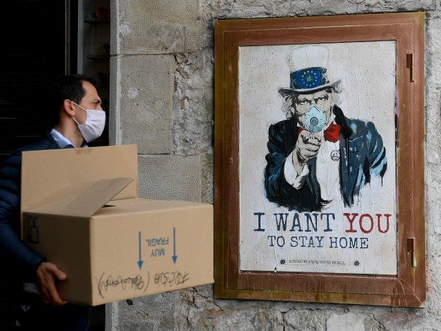 A man wearing a face mask walks past a poster by artist TVBoy featuring Uncle Sam and reading "I want you to stay home" in Barcelona on March 14, 2020 after regional authorities ordered all shops in the region be shuttered from today through March 26, save for those selling …