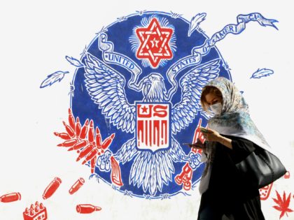 A woman, wearing a protective mask amid the COVID-19 pandemic, walks past a mural painted on the outer walls of the former US embassy in the Iranian capital Tehran on September 20, 2020. - Iran called on the rest of the world to unite against the United States, after Washington …