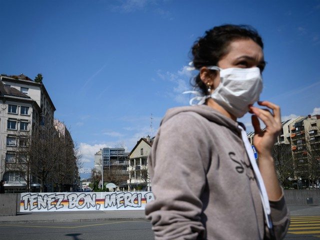 TOPSHOT - A woman wearing a protective face mask walks by a giant banner reading : "Hold on, thank you for everything" deployed in front of the Geneva University Hospitals (HUG) as a lockdown is in effect to prevent the spread of the COVID-19 caused by the novel coronavirus, in …