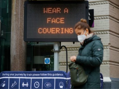A pedestrian walks past a sign displaying a message to wear a face covering, outside Chari