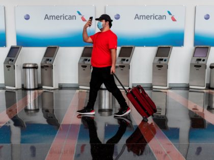 A passenger walks past empty American Airlines check-in terminals at Ronald Reagan Washington National Airport in Arlington, Virginia, on May 12, 2020. - The airline industry has been hit hard by the COVID-19 pandemic, with the number of people flying having decreased by more than 90 percent since the beginning …