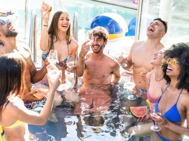 Side view of happy friends group drinking white wine champagne at swimming pool party - Luxury vacation concept with young guys and girls having fun in summer day at hotel resort - Warm bright filter - stock photo