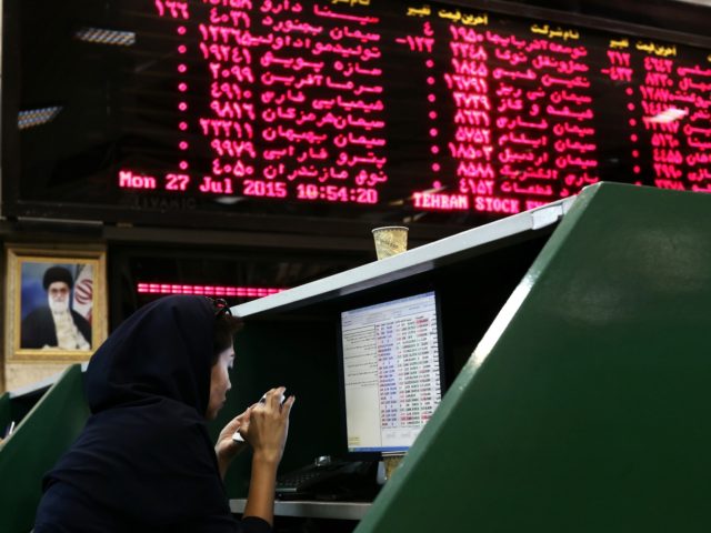 An Iranian dealer checks her mobile phone next to stock market activity boards at the stoc