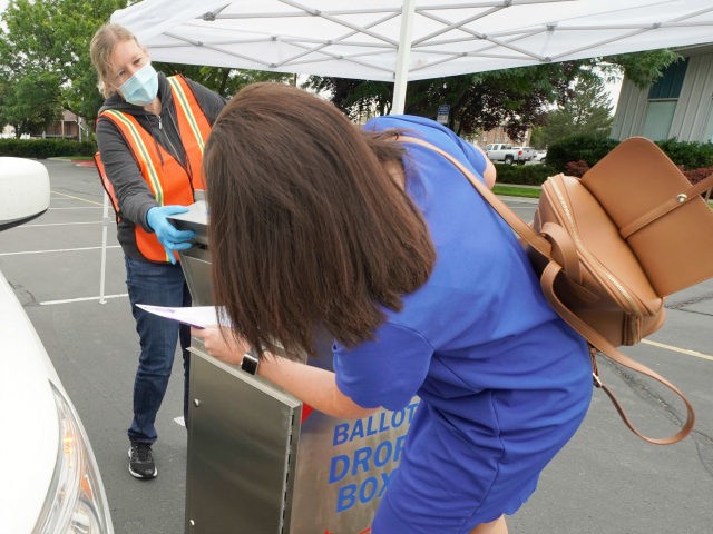 A woman is helped by an election worker to put her ballot in a box while voting from her c