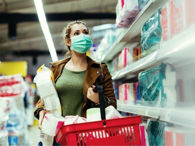 Young woman wearing face mask and making supplies of toilet paper while buying in supermarket in time of virus pandemic.