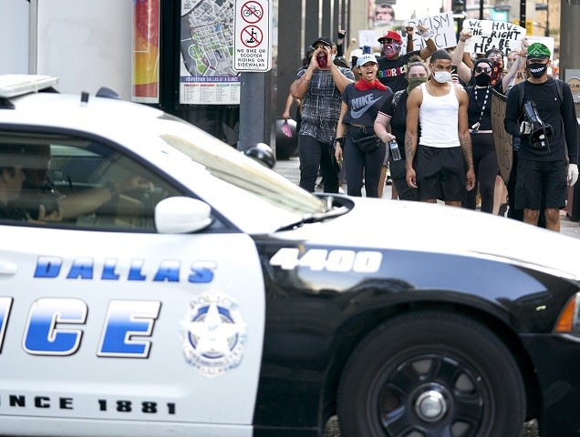 DALLAS, TX - JUNE 06: Demonstrators march past a Dallas Police car during a peaceful prote