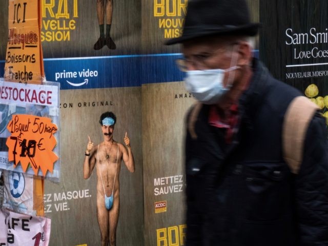 A man wearing a protective face mask walks past a shop selling masks as a poster of the film Borat by Sacha Baron Cohen is displayed in Paris,on the fourth day of a lockdown aimed at containing the spread of the novel coronavirus (Covid-19), on November 2, 2020. (Photo by …