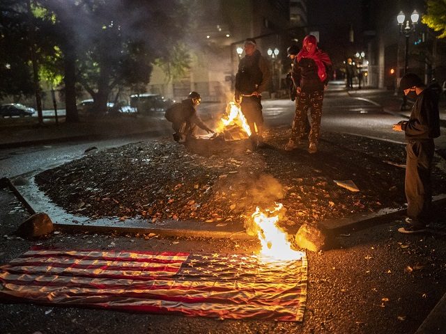 PORTLAND, OR - NOVEMBER 04: A small group of racial justice protesters watch a burning Ame