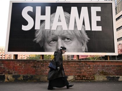 TOPSHOT - A woman wearing a protective face shield passes a billboard showing Britain's Prime Minister Boris Johnson in Manchester, north-west England on November 6, 2020, as the second lockdown comes into force in England. - A united effort to tackle spiking coronavirus infection rates has been called for as …