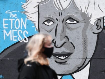 A woman wearing a mask because of the coronavirus pandemic walks past a mural depicting Britain's Prime Minister Boris Johnson on the front of a closed pub in Manchester, northwest England on November 10, 2020 during a second national coronavirus lockdown. (Photo by Oli SCARFF / AFP) (Photo by OLI …
