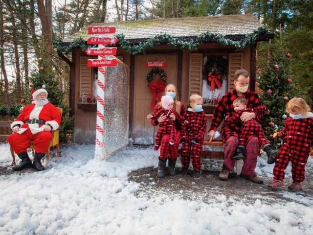 A family wears Christmas outfits as they pose for a photograph with Santa with plexiglas i