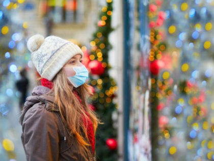 Girl wearing face mask on a Parisian street or at Christmas market looking at shop windows