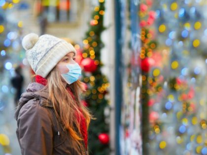 Girl wearing face mask at Christmas market looking at shop windows decorated for Christmas. Seasonal holidays during pandemic and coronavirus outbreak