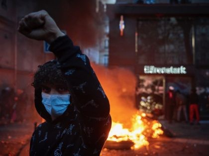 PARIS, FRANCE - NOVEMBER 28: A protestor stands outside a burning BMW showroom as demonstrations against the French Government's Global Security Law turn violent near Place de la Bastille on November 28, 2020 in Paris, France. France's lawmakers passed and adopted the bill known as article 24 of the “comprehensive …
