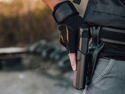 Close-up image of a man holding hand gun in holster on the belt.