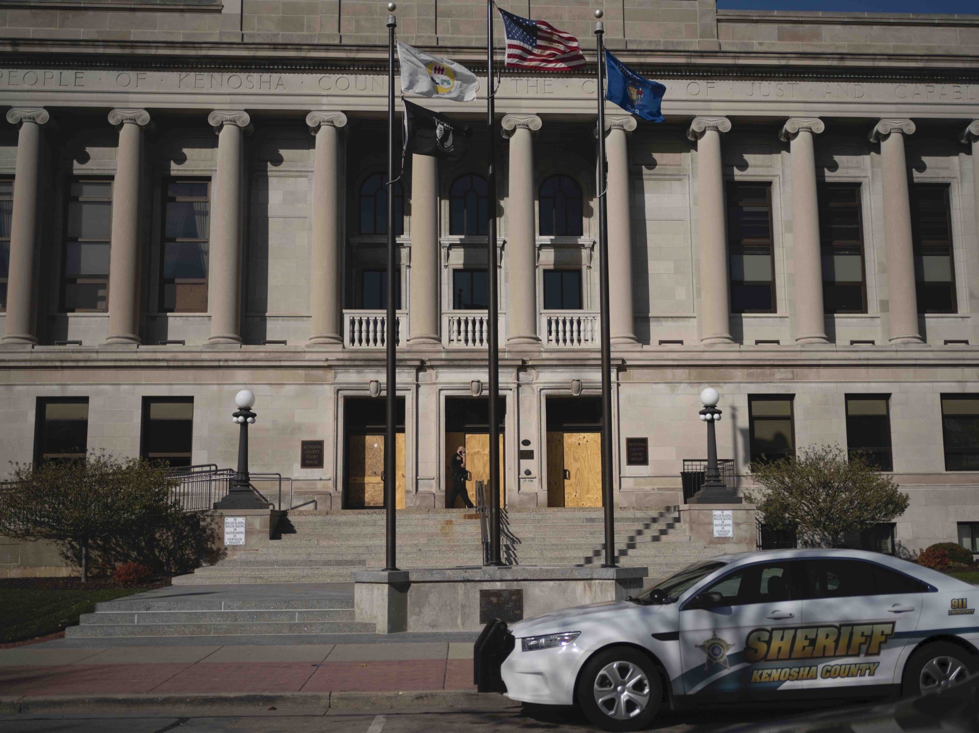 A police officer walks in front of the Kenosha County circuit court, Monday, Nov. 2, 2020, in Kenosha, Wis.. Bail was set at $2 million on Monday for a 17-year-old from Illinois accused of killing two men and wounding a third during an August protest in Kenosha, after the father of one of the victims told the court the defendant "thinks he's above the law" and would be a flight risk if freed before trial. (AP Photo/Wong Maye-E)