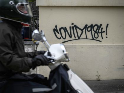 A man on a scooter passes by a graffiti reading "Covid 1984" as a reference to the novel 1