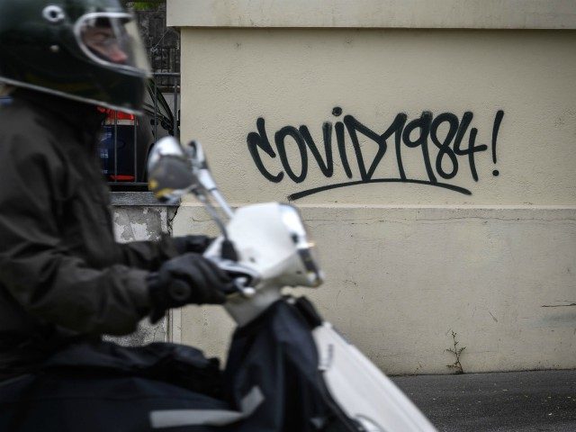 A man on a scooter passes by a graffiti reading "Covid 1984" as a reference to the novel 1984 by George Orwell on a wall in a street of Lausanne on May 12, 2020 amid the COVID-19 outbreak, caused by the novel coronavirus. (Photo by Fabrice COFFRINI / AFP) (Photo …