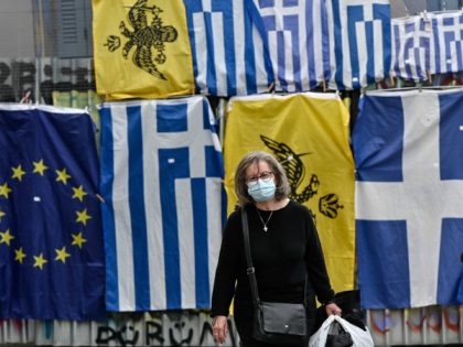A pedestrian wears a mask as she walks past EU, Greek and Byzantium flags in central Athens on November 3, 2020. - Athens has imposed a partial lockdown to stem the spread of the novel coronavirus (Covid-19) closing its cafes, bars, restaurants and museums. (Photo by LOUISA GOULIAMAKI / AFP) …