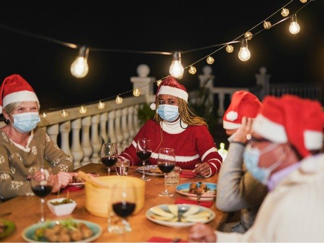 Multiracial senior people celebrate christmas together with dinner outdoor while wearing surgical face mask for coronavirus - stock photo