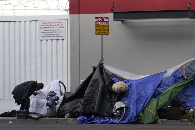 A man stands near tents set up on a sidewalk in San Francisco, Saturday, Nov. 21, 2020. Some counties in California are pushing ahead with plans to wind down a program that's housed homeless people in hotel rooms amid the pandemic, despite an emergency cash infusion from the state aimed …