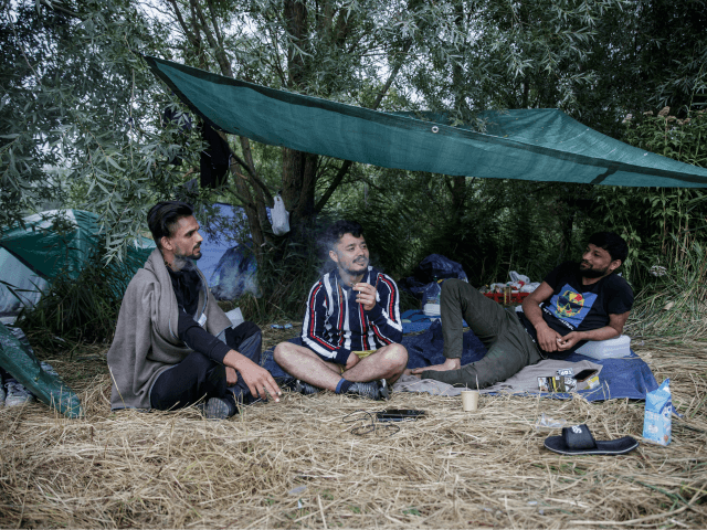 Migrants from Afghanistan sit under a semi-tent as they talk and smoke at a makeshift camp in the outskirts of Calais, northern France, on August 14, 2020. - The number of migrants crossing the English Channel -- which is 33,8 km (21 miles) at the closest point in the Straits …
