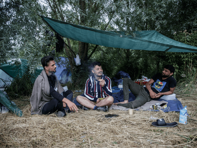 Migrants from Afghanistan sit under a semi-tent as they talk and smoke at a makeshift camp