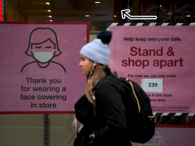 A pedestrian walks past posters advising customers to wear a face mask or covering due to