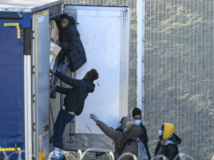 Migrants climb into the back of lorries bound for Britain while traffic is stopped upon wa