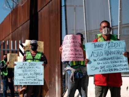 Migrants and advocates hold signs as they demonstrate by the US-Mexico border fence at the San Ysidro crossing port in Tijuana, Baja California state, Mexico, on December 18, 2020, to commemorate the International Migrants Day. (Photo by Guillermo Arias / AFP) (Photo by GUILLERMO ARIAS/AFP via Getty Images)