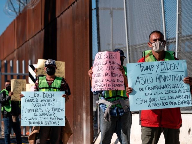 Migrants and advocates hold signs as they demonstrate by the US-Mexico border fence at the