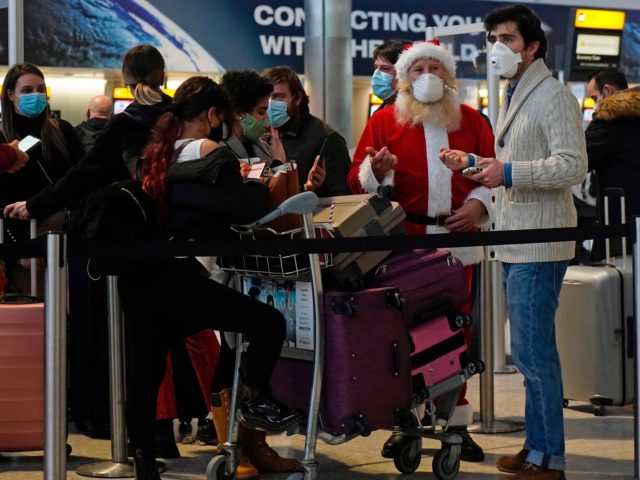 Travellers, one dressed in a Father Christmas outfit and all wearing face coverings, queue with their luggage in the departures hall at Terminal 2 of Heathrow Airport in west London on December 21, 2020, as a string of countries around the world banned travellers arriving from the UK, due to …
