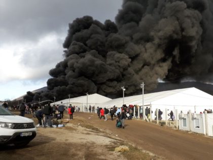 Refugees leave a camp as a fire burns, near the northwestern village of Lipa, Bihac region
