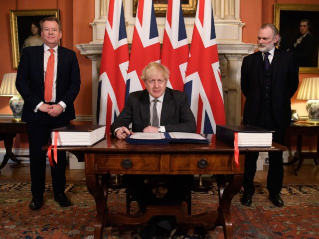 Britain's Prime Minister Boris Johnson (C) flanked by UK chief trade negotiator David Frost (L) and British Ambassador to the EU Tim Barrow (R) signs the Trade and Cooperation Agreement between the UK and the EU, the Brexit trade deal, at 10 Downing Street in central London on December 30, …
