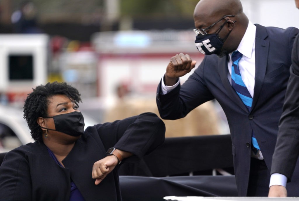 ATLANTA, GA - DECEMBER 15: U.S. Democratic Senate candidate Raphael Warnock (R) bumps elbows with Stacey Abrams (L) during a campaign rally with U.S. President-elect Joe Biden at Pullman Yard on December 15, 2020 in Atlanta, Georgia. Biden’s stop in Georgia comes less than a month before the January 5 runoff election for Senate candidates Jon Ossoff and Raphael Warnock as they try to unseat Republican incumbents Sen. David Perdue and Sen. Kelly Loeffler. (Photo by Drew Angerer/Getty Images)