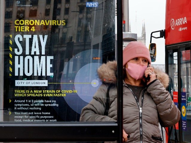 A passenger wearing a mask because of the coronavirus pandemic talks on the telephone waiting at a bus stop with a government message about the coronavirus tier 4 restrictions urging people to stay home in London on December 29, 2020. - England is "back in the eye" of the coronavirus …
