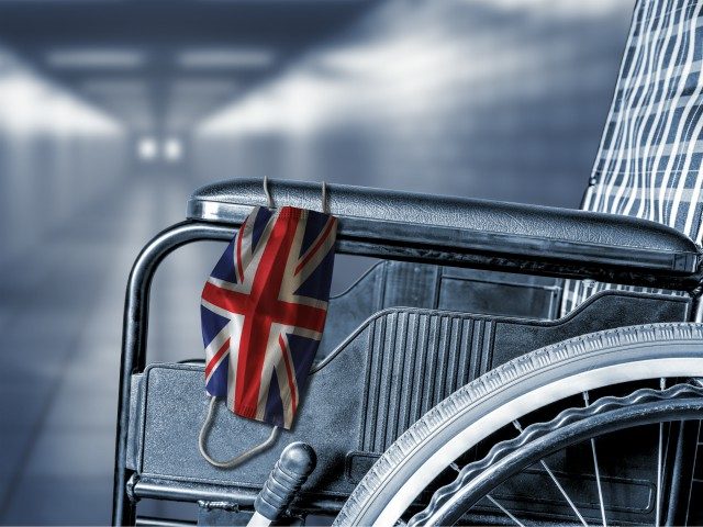 Flag of UK United Kingdom on face mask hanging on empty wheelchair in hallway of British hospital or retirement nursing care home with copy space.