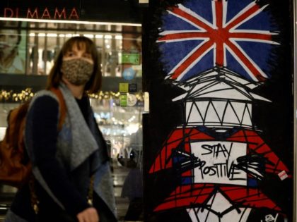 A woman wears a facemask as she walks past graffiti on Victoria Street in central London o