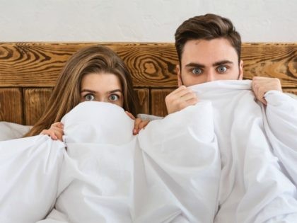 Fear concept. Husband and wife hiding at blanket and watching movie - stock photo