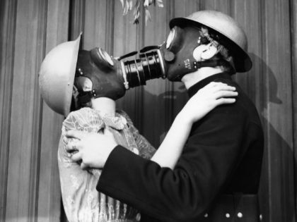 A couple kissing under the mistletoe, wearing gas masks. (Photo by Fox Photos/Getty Images)
