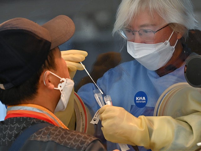 A medical staff member wearing protective gear takes a swab from a visitor to test for the