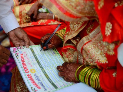 An Indian Muslim bride (R) places her signature on a certificate as she participates in a mass marriage in Ahmedabad on December 3, 2018. - Some 65 Muslim couples were wedded in the mass marriage ceremony. (Photo by SAM PANTHAKY / AFP) (Photo credit should read SAM PANTHAKY/AFP via Getty …