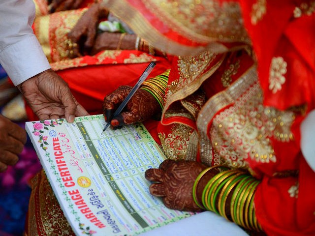 An Indian Muslim bride (R) places her signature on a certificate as she participates in a