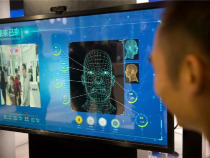 A man watches as a visitor tries out a facial recognition display at a booth for Chinese t