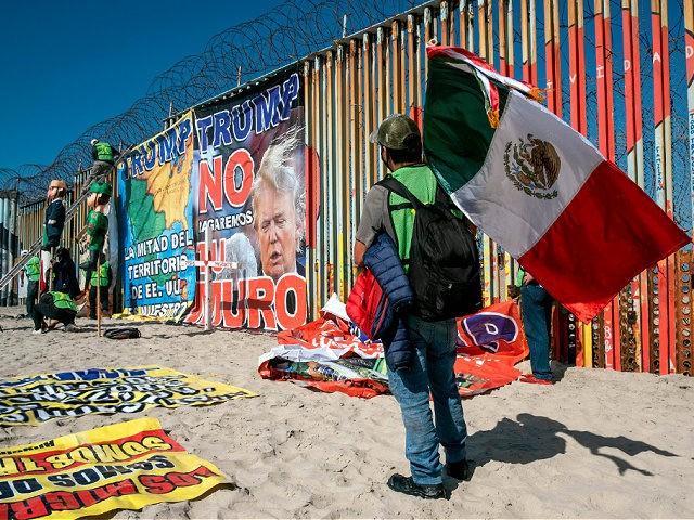 A demonstrator holds a Mexican flag as others hang banners from the border fence during a protest against US President Donald Trump's migration policies, in Playas de Tijuana, Baja California state, on the border with the US, on October 31, 2020 - Trump said in an interview with Mexican newspaper …