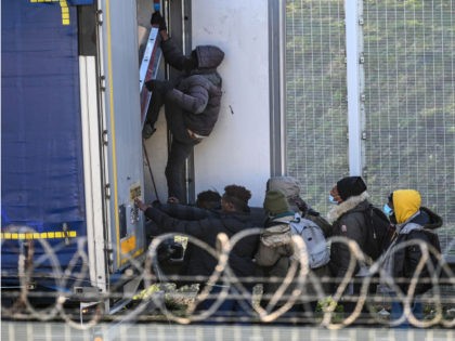 Migrants climb into the back of lorries bound for Britain while traffic is stopped upon wa