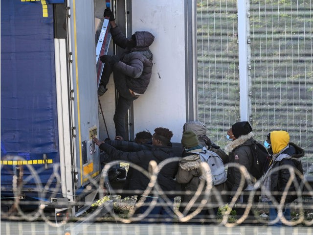 Migrants climb into the back of lorries bound for Britain while traffic is stopped upon waiting to board shuttles at the entrance to the Channel Tunnel site in Calais, northern France, on December 10, 2020. - The French port of Calais continues to attract migrants from the Middle East and …