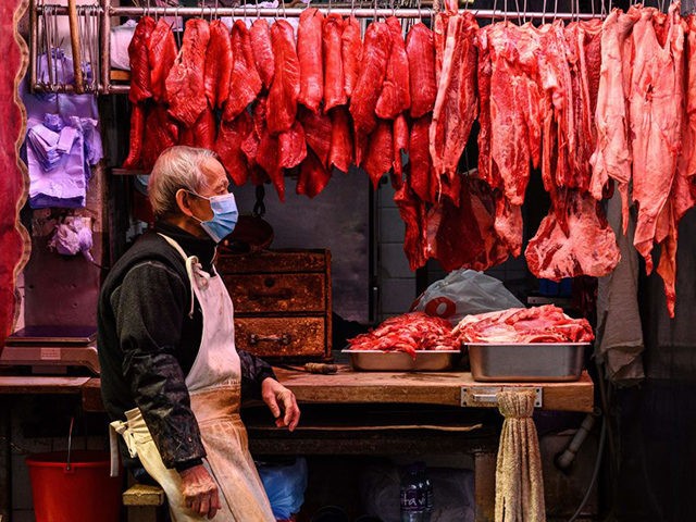A butcher sits next to fresh meat hanging on display as he waits for customers at his stre